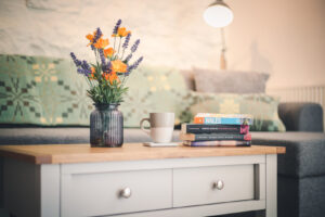 A picture of a coffee table with books, flowers and a mug of coffee placed on it. In the background, there is a comfortable sofa.