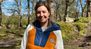 A picture of writer, Casia Wiliam, wearing a colourful fleece in the forest.