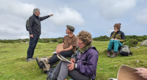 People writing outdoors. A man is pointing towards something in the distance.